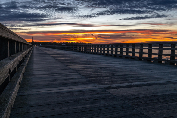 A photograph of sunset over the long, wooden Powder Point Bridge. 
