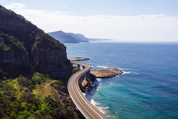 View of the Sea Cliff Bridge from the unofficial lookout point, depicting the bridge winding along the coastline between cliffs and the ocean in New South Wales, Australia.