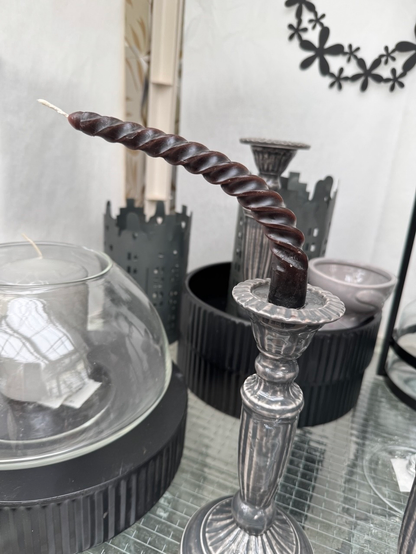 Das Bild zeigt eine verbogene, spiralförmige Kerze in einem silberfarbenen Kerzenhalter. Die Kerze ist braun und deutlich zur Seite gebogen, vermutlich durch Wärme oder falsche Lagerung verformt.