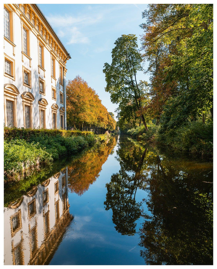 Links ein historisches Gebäude, mittig ein Kanal mit dunklem Wasser, rechts Bäume. Die Szene spiegelt sich im dunklen Wasser.