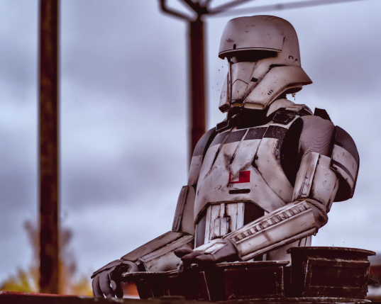 Ein Star Wars Sturmtruppler steht in der Dachluke eines Fahrzeuges und schaut reglos in die Ferne. Er hat sich offenbar schon lange nicht mehr bewegt, denn an Helm und Rüstung sind Spinnweben zu erkennen. Hinter dem Sturmtruppler sind die Pfosten einer Überdachung zu sehen und grauer Himmel. Die Rüstung des Sturmtrupplers ist schmutzig und ungepflegt. 
.
A Star Wars stormtrooper stands in the roof hatch of a vehicle and stares motionless into the distance. He has obviously not moved for a long time, as cobwebs can be seen on his helmet and armour. Behind the stormtrooper, the posts of a canopy and a grey sky can be seen. The stormtrooper's armour is dirty and messy. 
.