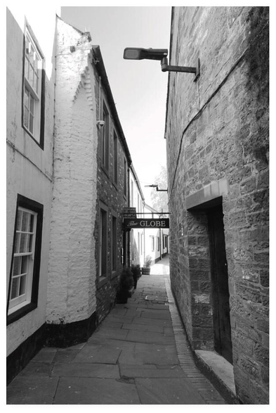 Black and white portrait photograph of a flagstoned alleyway with a pub sign for The Globe.