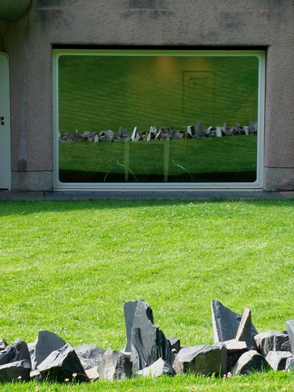 Im Fenster der historischen Villa "Waldfrieden" im Skulpturenpark in Wuppertal spiegelt sich die Arbeit "Basalt Slate" des LandArt-Künstlers Richard Long. Das 2015 entstandene Werk, eine gerade Linie aus schroffen, spitzen Basalt- und Schieferbrocken, liegt in der Wiese auf der Rückseite der Villa. 
Die kantige Skulptur bildet einen starken Kontrast zum organischen Gebäude, in dem es keine rechten Winkel gibt.