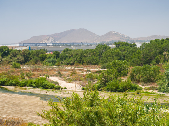 Santa Ana River in front of a hazy and dry hill; warehouses are by the foothill.