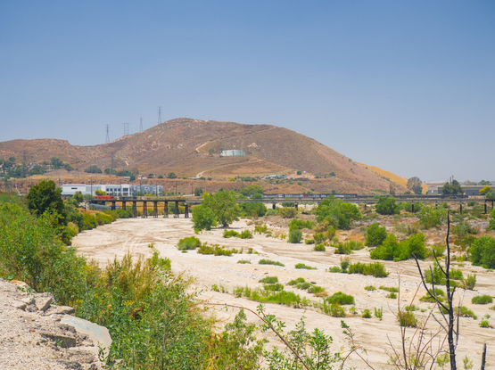 In the distance, a bridge crosses the dry riverbed of Santa Ana River, beneath a dry hill.