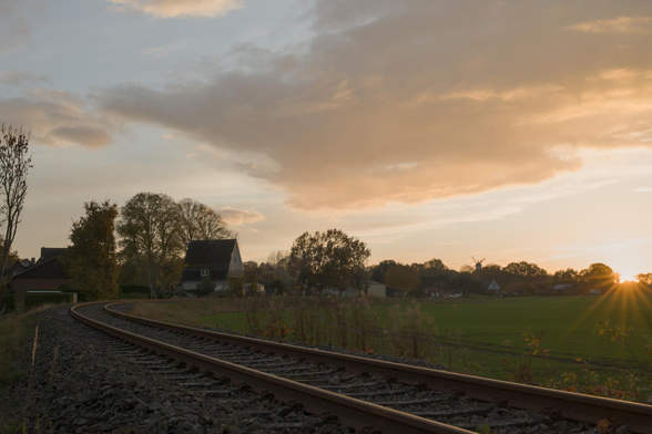 Blick auf eine geschwungene Eisenbahnstrecke bei Sonnenuntergang mit Häusern und Bäumen im Hintergrund.
