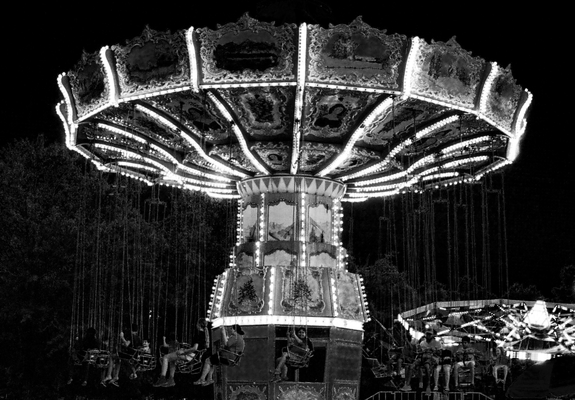 A black and white photo of a swing ride at the carnival with the riders loaded on and ready for the ride to start.