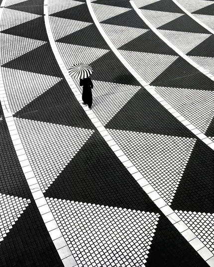 tenue par une silhouette noire, une ombrelle au motif spiralé tourne sur elle-même tout parcourant une orbite sur une rosace aux cercles concentriques pavée d'une frise au motif de triangles alignés tête-bêche