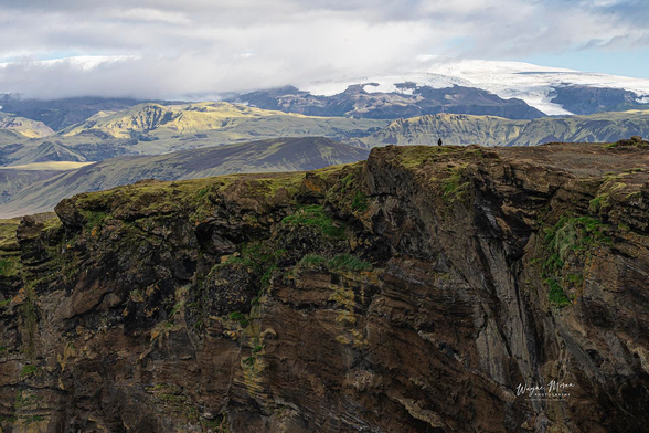 Dyrhólaey Iceland Clifftop and Mýrdalsjökull Glacier View

Standing on the edge of the Dyrhólaey cliffs in southern Iceland, you witness a world shaped by ancient lava flows, relentless North Atlantic winds, and the power of glaciers and volcanoes working over thousands of years. This vantage point rises high above the crashing waves below, where sheer basalt walls plunge into the sea and vibrant moss clings to every fracture in the rock. The landscape feels raw, untouched, and wonderfully alive.

In the distance, the vast ice dome of Mýrdalsjökull stretches across the horizon, glowing beneath soft light and shifting clouds. This glacier rests above the mighty Katla volcano, a powerful force that has shaped the region’s dramatic contours. Rolling volcanic hills and black sand plains unfold toward the horizon, creating a tapestry of greens, golds, and volcanic earth tones that capture the essence of Iceland’s south coast.

A tiny human figure stands at the clifftop, offering a humbling sense of scale and awe. That small silhouette reminds us just how immense and majestic this world is.

Image:
https://fineartamerica.com/featured/dyrholaey-clifftop-and-myrdalsjokull-glacier-view-wayne-moran.html

Read more:
https://waynemoranphotography.com/blog/chasing-light-across-iceland-our-21-day-adventure/

#Dyrhólaey #Dyrholaey #Cliffs #mountains #Glacier #Iceland #travelPHotogrpahy #Landscape #art #fineart 

#ayearforart #buyintoart
