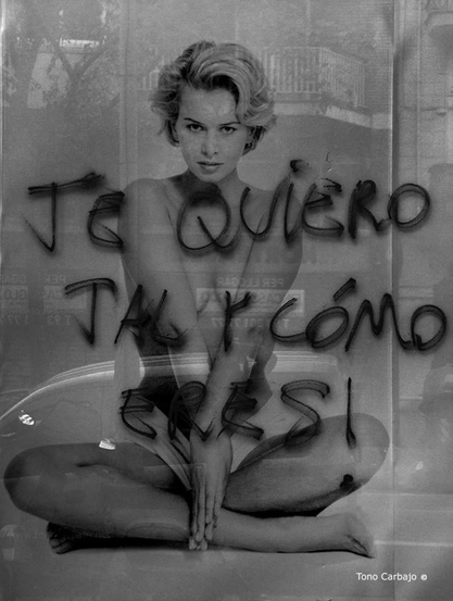 La foto muestra a una mujer joven, sentada en posición de loto o con las piernas cruzadas, con las manos juntas . Tiene el torso desnudo y el pelo corto.
Sobre la imagen, hay un texto escrito a mano con spray, sobre el cristal del escaparate. El cristal refleja un poco la calle. 
El texto dice: "Te quiero tal y cómo eres"