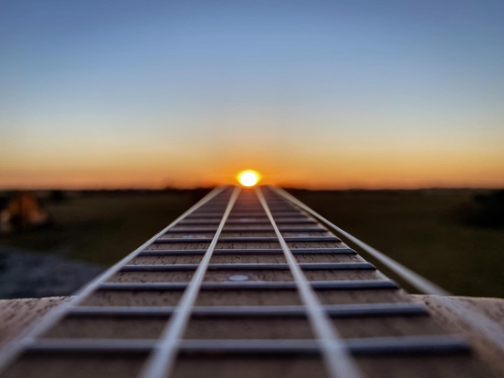 Close-up of a ukulele’s neck leading toward the horizon, with the setting sun perfectly aligned at the end of the strings.