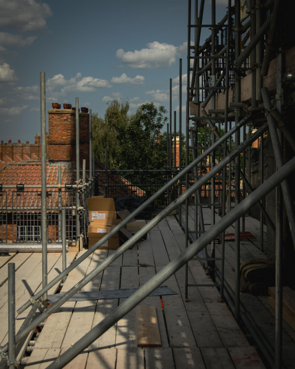 Scaffolding around the church in the sunlight looking over the roof and chimney of an adjacent house.  