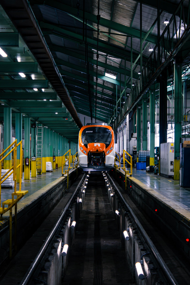 A front view of a Civia EMU that's just been inspected and cleaned, sitting on top of some rails inside a trench. It looks very shiny.
