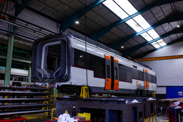 The middle car of a Renfe class 465 EMU, inside the warehouse, with the interior disassembled and the bogies removed. The gangway accordion is visible on one end of the car. They're performing maintenance tasks on it.