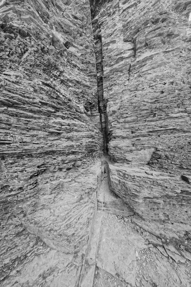 A great big crack in a shale rock formation is seen running right down the middle of the frame,  on both sides of the crack numerous fine layers are stacked on top of each other