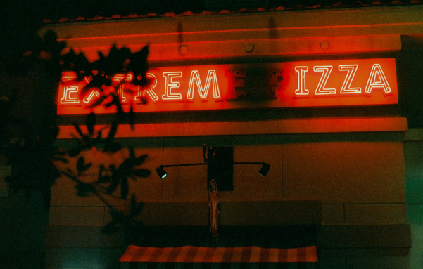 A photo of a neon sign over a pizza restaurant with not all letters lit up.  It now says "Extrem IZZA".