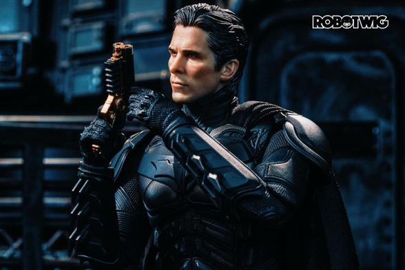 Bruce Wayne unmasked in Batman suite checks his grappling hook down in the Batcave 