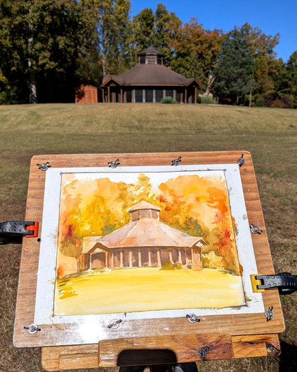 Third shot, A new painting started inside the same clamp board. This one depicts an octagonal building at the top of a small hill with trees in the background. The overall tone of the pieces is orange with nuanced reds, yellows, and greens.