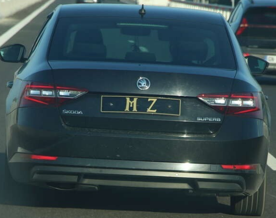 A black car on a highway with the numberplate "MZ" in golden letters on black.