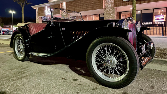 Photo of a black late-1940s MG TC sports car at night in a parking lot.