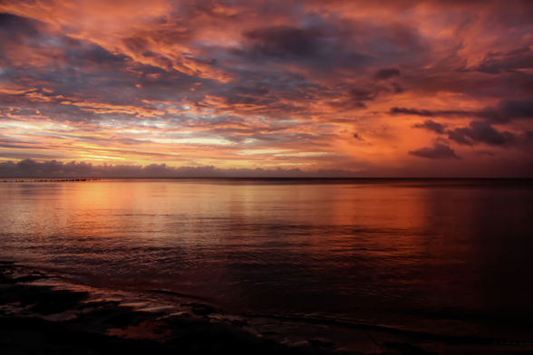 Ein Sonnenuntergangsszenario an der Ostsee. Der Himmel mit den Wolken "glühen" in den Farben Orange und Rot. Das spiegelt sich auf der verhältnismässig ruhigen Ostsee wieder.