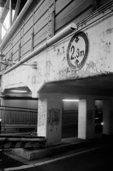 역곡역 굴다리를 도보에서 찍은 흑백사진. 1번 사진과는 다른 방향. 낡은 굴다리 입구에는 '2.3m 높이제한' 표지판이 붙어있고, 안쪽에는 굴다리를 지탱하는 네모난 기둥과 도보 안전 울타리가 보인다. 높이제한 표지판 앞쪽에는 쇠사슬에 매달린 가로대가 있다.