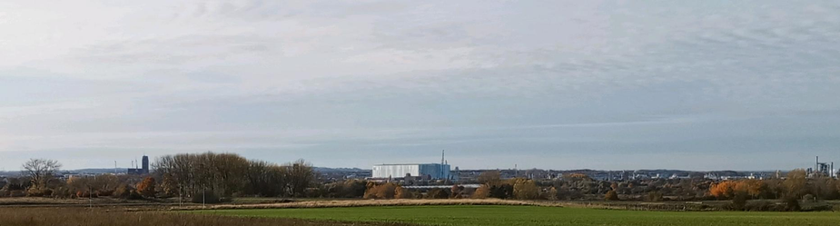 Panoramic view of Wismar with the  shipyard building hall and crane and smaller harbour cranes in the centre an then medival church tower of the former church of St.Mary to the left. Pale autumn midday  sunlight under a cloudy sky over fields, trees and distant buildings.