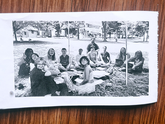 dithered photo of HTML day from a thermal printer. a crowd of people sitting under a tent on picnic blankets. 
