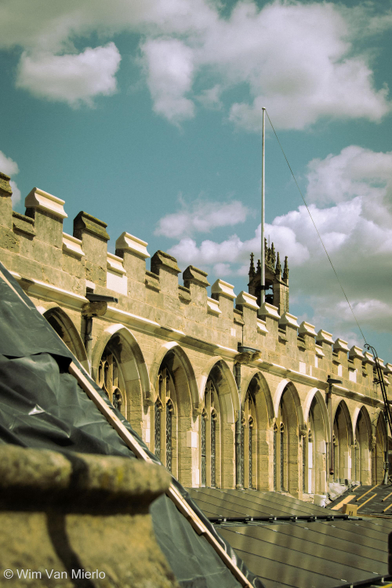 View along the rooftop of a church: the top part of the nave with arched windows, with a flagpole and small spire.  Also visible are solar panels.