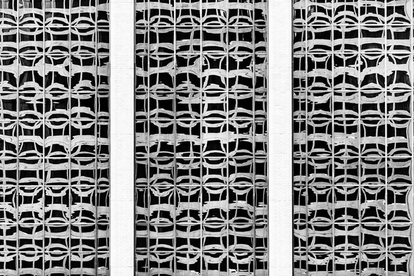 A high-contrast, black and white photograph image of one building's distorted reflection in another building's window. The image is dominated by three vertical panels that extend from the top to the bottom edge. These panels are separated by narrow, white vertical strips of brick. The main feature of each panel are the dark windows which reflected a distorted view of the building across from them. The overall effect is an abstract, graphic composition.