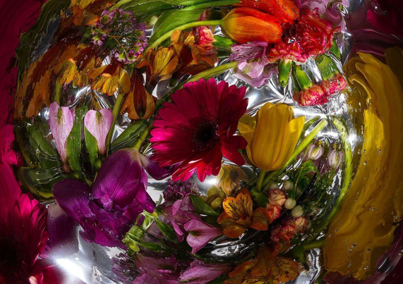 Vibrant flowers in various colors, including pinks, yellows, and oranges, submerged in shimmering water with bubbles.