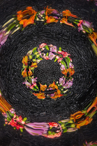 Colorful flower arrangements swirl in water, creating an abstract pattern against a dark backdrop.