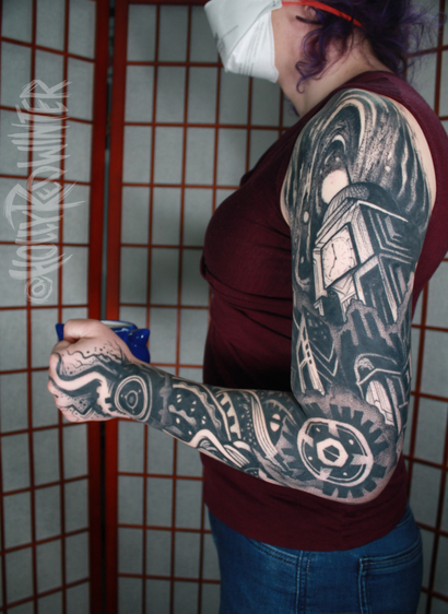 the photo shows the left arm of the author, shown from the outside with the arm bent at 90 degrees holding a mug. The author has a finished tattoo sleeve that is black and grey in an "art-deco" style that depicts a galaxy at the top on the shoulder, a clocktower/observatory below with a cityscape leading down into mechanical pieces of gears, wires, and tubing down to the hand