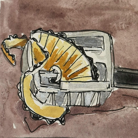 A metal two hole pencil sharpener with a number two pencil being sharpened in the smaller of the two holes. A spiral of pencil sharpening is coming out of the other end.