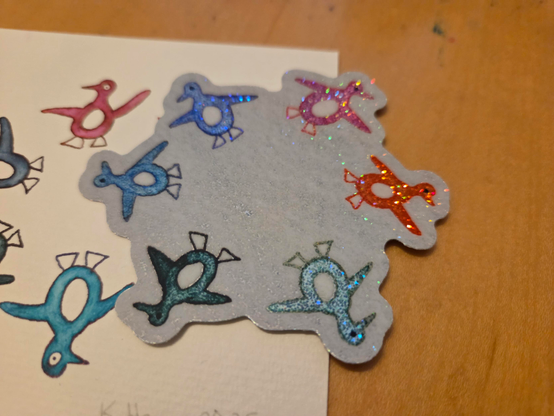 a sparkly sticker with penguins and a hand drawn piece on watercolor paper that inspired the sticker art.
