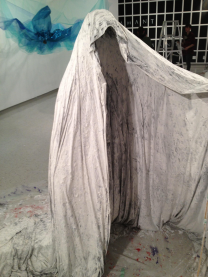 A cloak stands suspended, rigid like stone, and with the shape of a person, and yet no one resides within. Ghostly, grey, empty. 