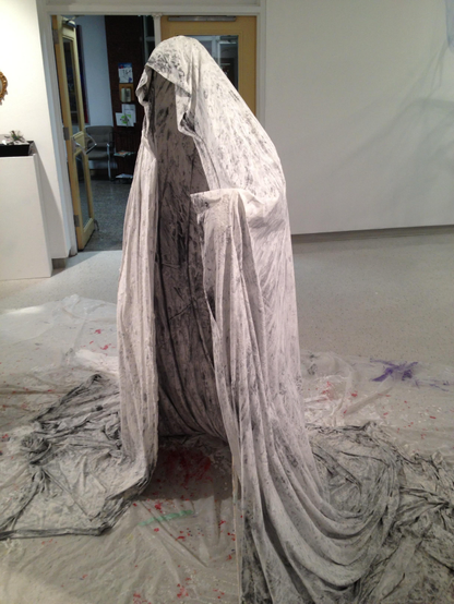 An empty cloak made of plaster and fabric stands in an open room. 
