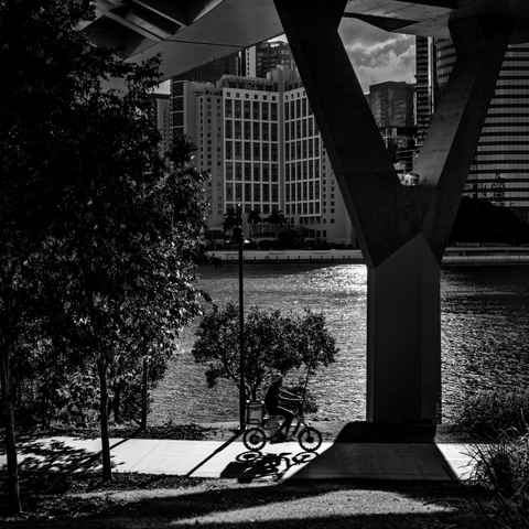 Person on a bike going under a large bridge in Brisbane.  It's high contrast black and white picture