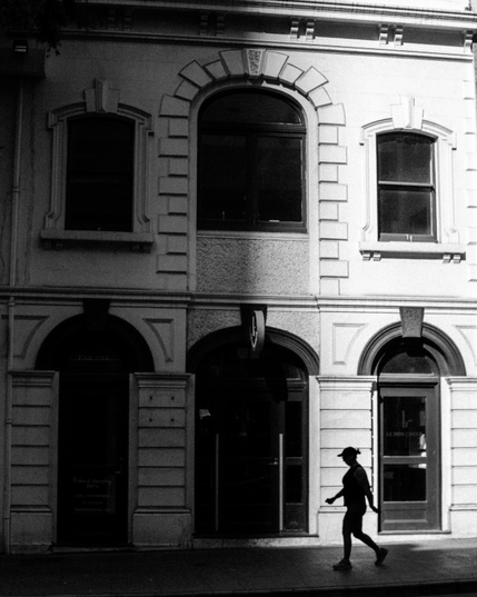 A person walking past an old building in the centre of Brisbane.  Its high contrast black and white picture