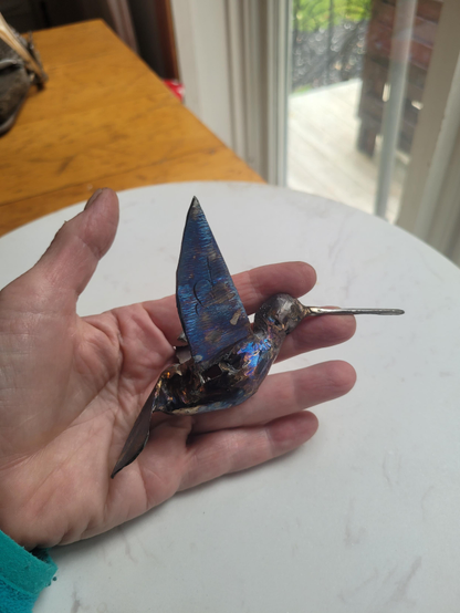 Boumboum Chevalier 

Un colibri grandeur nature, à suspendre, est dans ma main. Il est en rebut d'acier. J'ai réussi à mettre de la couleur avec une torche. C'est difficile. J'ai bien réussi sur ce petit. On voit des reflets bleus et mauves partout sur le petit oiseau. On peut mettre jeune, bleu ou mauve et je ne contrôle pas tellement la technique de sorte que la couleur est encore un peu aléatoire. 