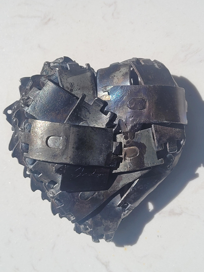 Solide
Un coeur en rebut d'acier fait de morceaux dont je n'ai aucune idée de l'utilité originale. Ce sont tous des morceaux pareils, rectangulaires d'environ 15cm de long x 5 cm de large. D'un côté j'ai mis le contour avec un morceau de scie à chaîne. L'autre côté est d'ailleurs à moitié fait avec des bouts de scie à chaîne. L'autre moitié est faites de clous. 