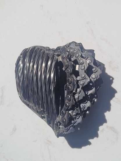 Solide
L'autre côté du coeur. D'un côté des clous tournés sont alignés côte à côte  et de l'autre côté, des bouts de scie à chaîne sont imbriqués comme des poupées russes. 