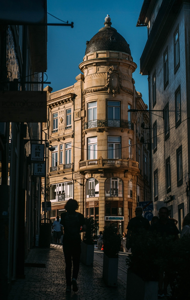 view from a street in the shadow, we see some people silhouettes from the back and at the end of the street an old town building in the sunlight.