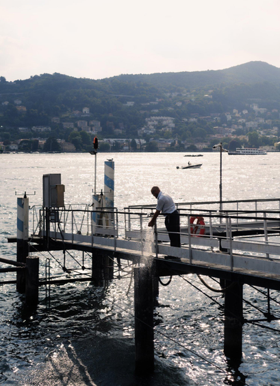 A man in a uniform washes his hands under a water stream coming out of a pipe on a pier.