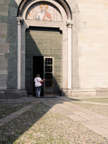 A woman enters the gate of a church in a shadow area while the rest of the scene is brightly lit by the sun.