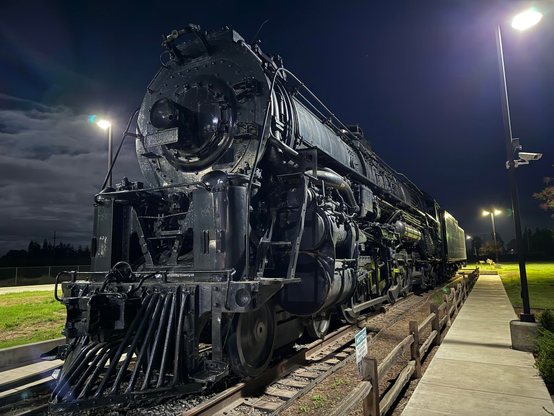 A steam locomotive at night, lit by nearby light poles.
