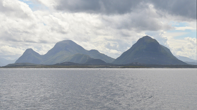 A photo of water leading into mountains. The sky is filled with clouds.