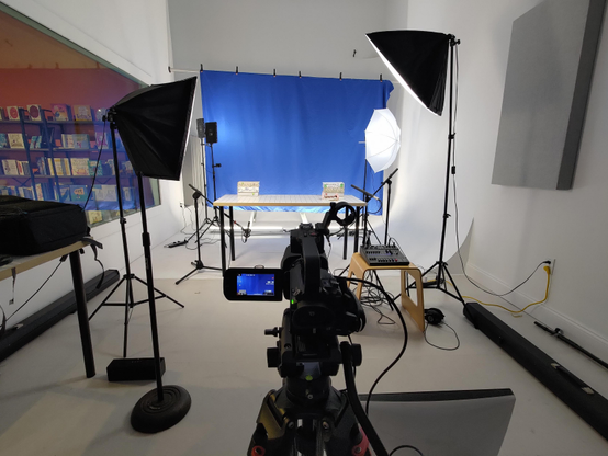 The studio set up for a day of shooting. At the back is a blue screen since two of our main characters are predominantly green. Various lights are set up to light the blue screen and the talent. Down in front is the audio mixer for capturing voice performance, and the camera which is outputting to an external monitor so the puppeteers can have a real-time view of their performance.