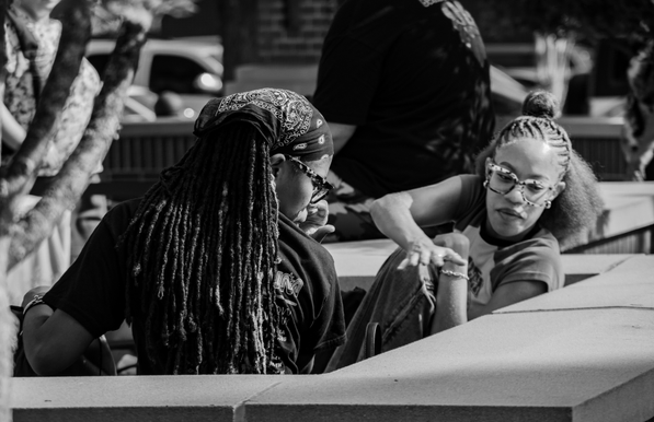 Two women sitting on an unseen bench.  Something on the wall in back of them has gotten their attention and they've both turned to look at it.