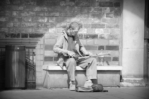 A homeless musician playing a self-made guitar - strings strung across the length of a common shovel - in Bremen. Copyright Urban Camera 2024